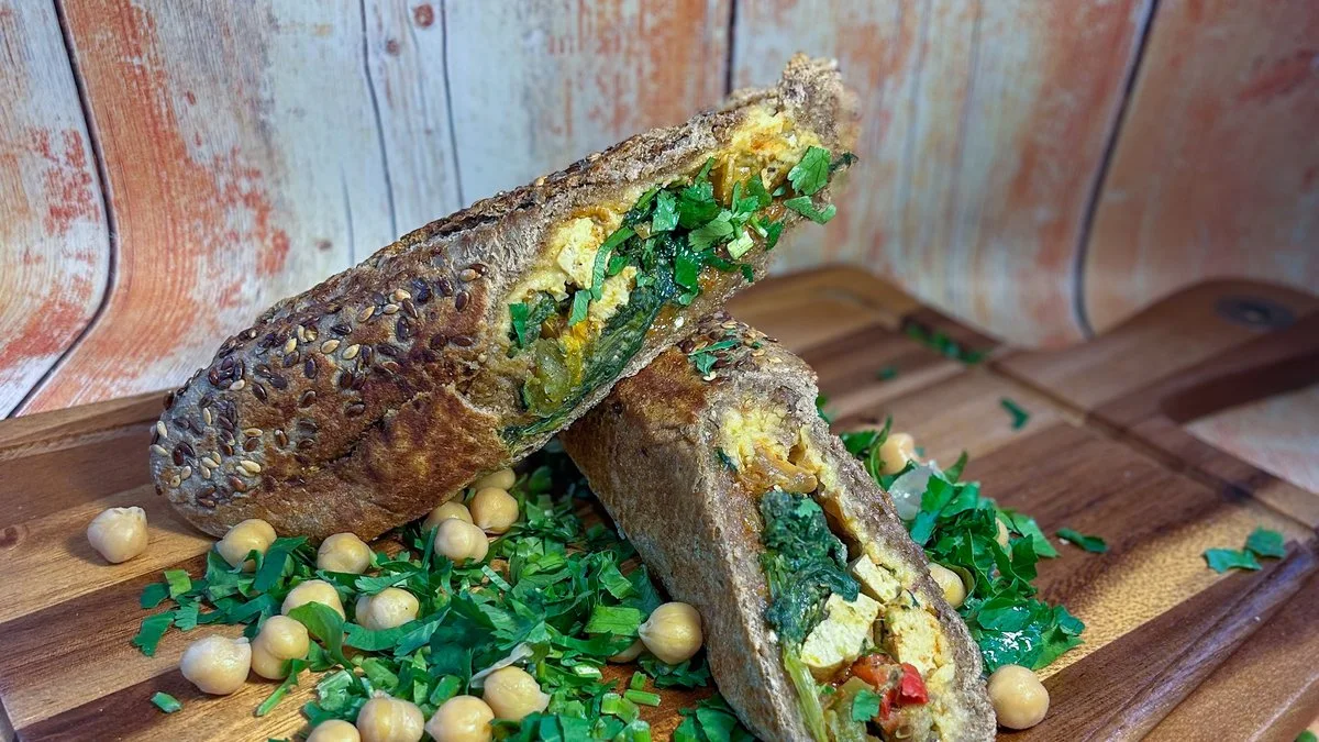 Hummus Sapiens wholegrain baguette cut open with hummus, spinach, tofu and coriander