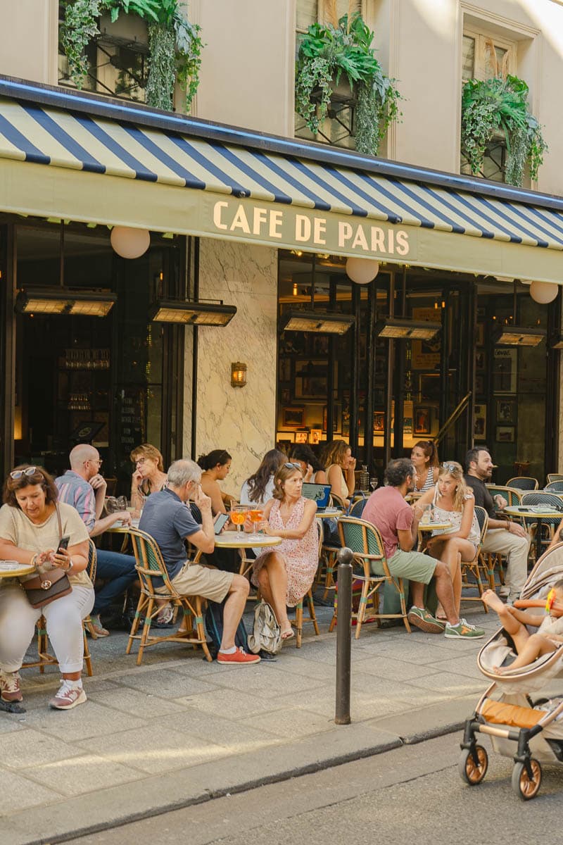 La terrasse animée du Café de Paris sous son store rayé rue de Buci