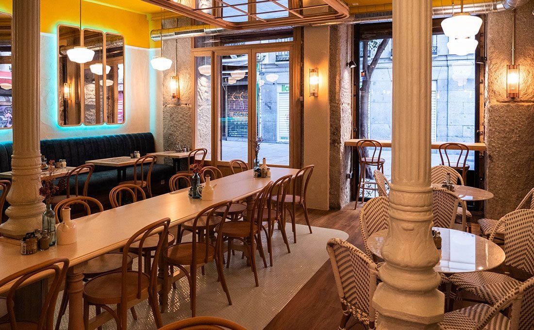 Interior real de Mimi’s Crêperie con paredes amarillas, neón turquesa y mesas de madera